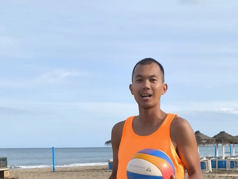 Jugador con la camiseta naranja del torneo y un balón en la playa